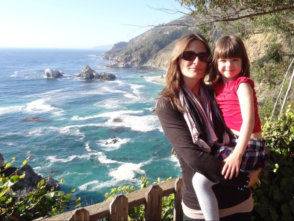 Picture of Gigi holding a little girl overlooking a spectacular California seashore view.